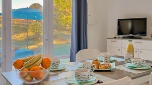 A dining area with a table set for breakfast, including fruits, croissants, and coffee cups.