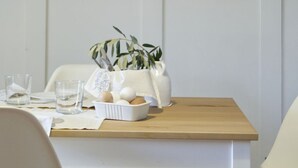 A dining table with chairs, a pitcher, a bowl of eggs, and a plant. There are framed pictures on the wall above the table.