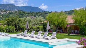 A pool area with lounge chairs, a view of a hillside with buildings, and a clear sky.