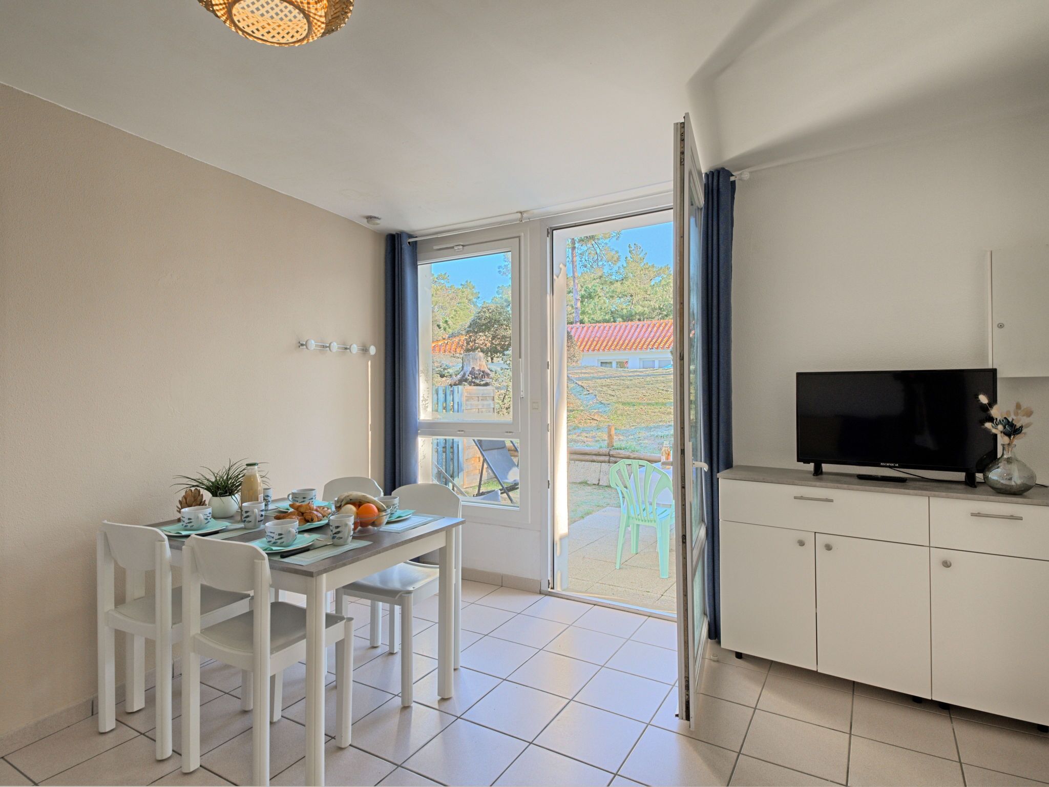 Un'area pranzo con un tavolo apparecchiato per due, una TV su un mobile e una porta scorrevole in vetro che dà su uno spazio all'aperto.