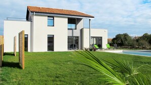 A modern two-story house with a tiled roof, a swimming pool, and a well-maintained lawn.