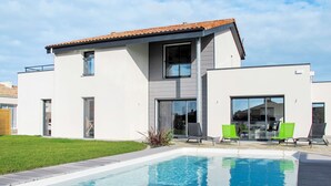A modern two-story house with a swimming pool, a patio with lounge chairs, and a well-maintained lawn.