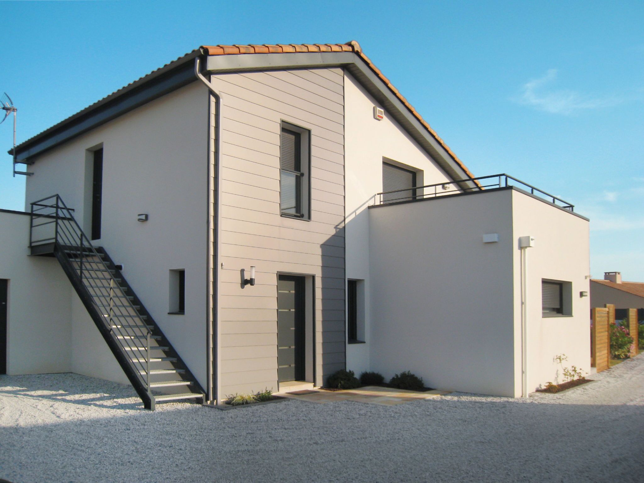Un bâtiment moderne à deux étages, avec une façade grise, un escalier sur le côté gauche et un petit balcon sur le côté droit.