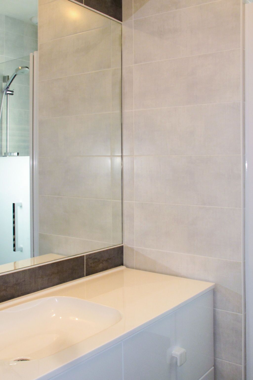 A modern bathroom with a large mirror, a white sink, and tiled walls.