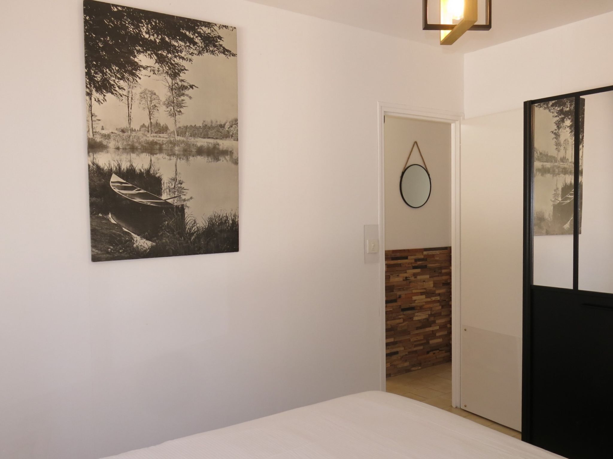 A bedroom with a bed, a wall-mounted mirror, and a door leading to a bathroom.