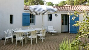 Eine Terrasse mit Tisch, Stühlen und einem gestreiften Sonnenschirm, sowie einer blauen Tür.