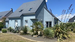 Ein zweistöckiges Haus mit grauem Dach, einer Satellitenschüssel und einem Garten mit verschiedenen Pflanzen.