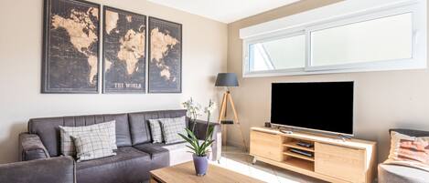 Ein modernes Wohnzimmer mit einem grauen Sofa, einem Holztisch, einem Fernseher und einer Wandkunst mit einer Weltkarte.