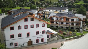 Un immeuble à plusieurs étages, doté d’une façade blanche et de cadres de fenêtres rouges, portant l’inscription « Mitterwirt ». Il possède un balcon au deuxième étage et un espace extérieur abrité avec des sièges.