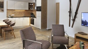 Une cuisine moderne agrémentée d’éléments en bois, un coin repas avec des chaises et un espace de vie doté d’un téléviseur et de paires de skis accrochés au mur.