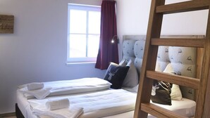 Un lit superposé avec une échelle en bois, une fenêtre avec des rideaux et un lit avec une literie blanche et un coussin à motif de cerf.