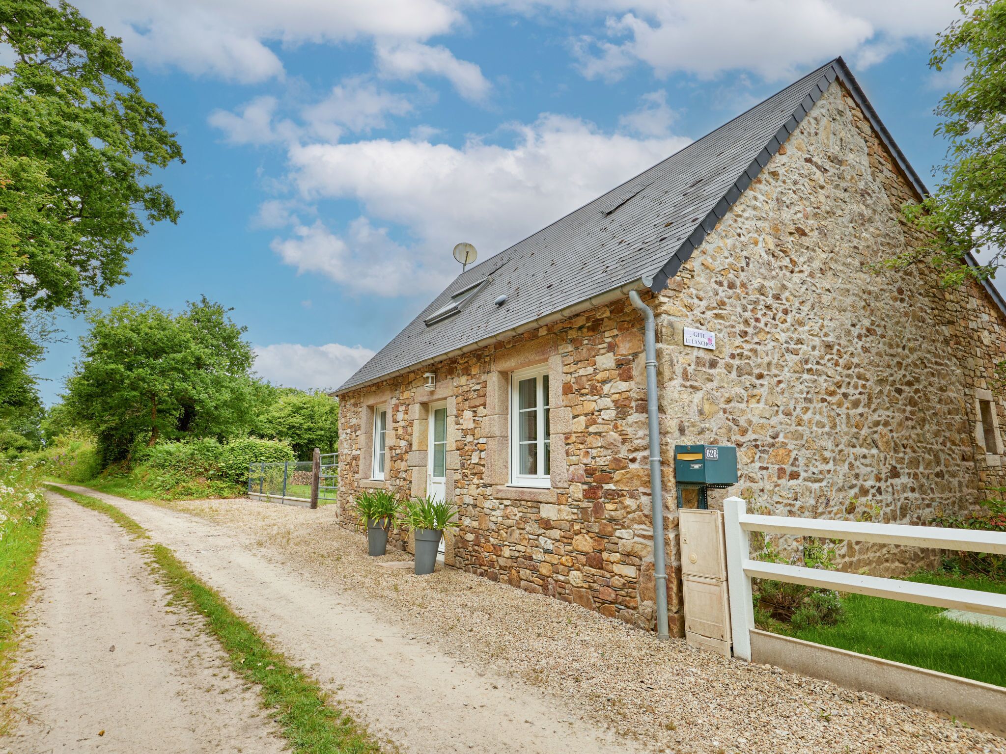 A stone building with a gravel driveway, a white fence, and potted plants.
