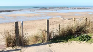 Una playa arenosa con vista despejada al mar, una cerca de madera y algo de vegetación.