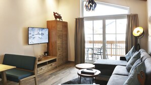 Uma sala de estar acolhedora com sofá, poltrona, armário de madeira, televisão e varanda com vista.
