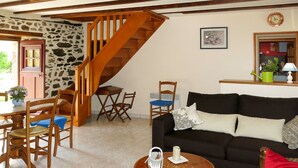 Un salon chaleureux avec un escalier, des meubles en bois, un canapé noir et un coin repas comprenant des chaises et une table.
