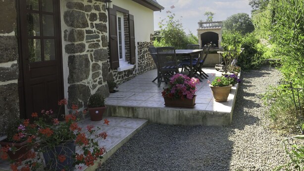 Un bâtiment en pierre doté d’un patio carrelé, de sièges en plein air et de plantes en pot.