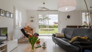 A modern living room with a sofa, coffee table, and a TV. There is a window with curtains, a lamp, and a vase with flowers.