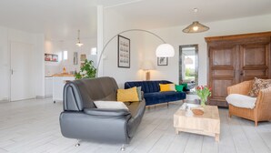 A modern living room with a grey sofa, a blue sofa with yellow cushions, a wooden coffee table, and a wicker chair.