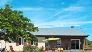 A house with a tiled roof, a covered patio with a bench, and a lawn.