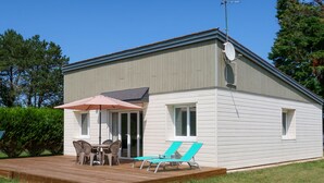 Une petite maison de plain-pied avec un patio, une table et des chaises, ainsi que deux fauteuils de jardin.