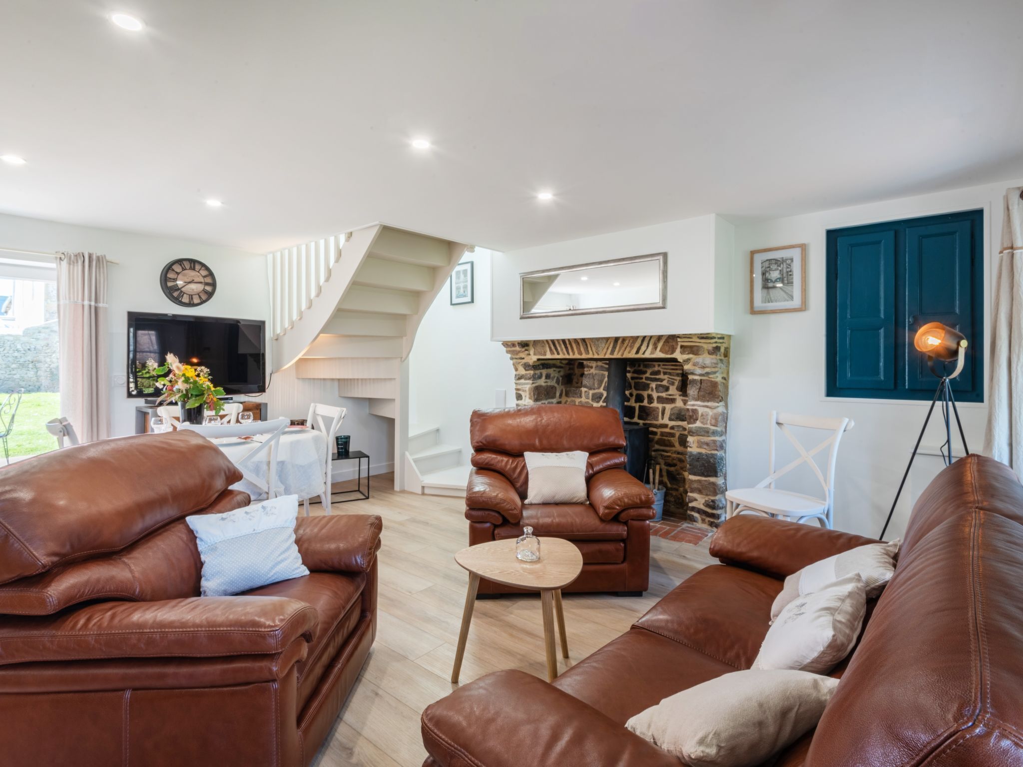 A spacious living room with leather sofas, a stone fireplace, and a staircase leading to an upper level.