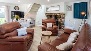 Ein großzügiges Wohnzimmer mit Ledersofas, einem Steinkamin und einer Treppe, die in eine obere Etage führt.