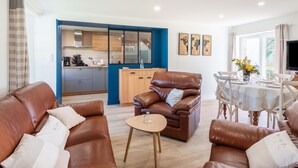 Ein modernes Wohnzimmer mit Ledersofas, einem Esstisch und einer Küche im Hintergrund.