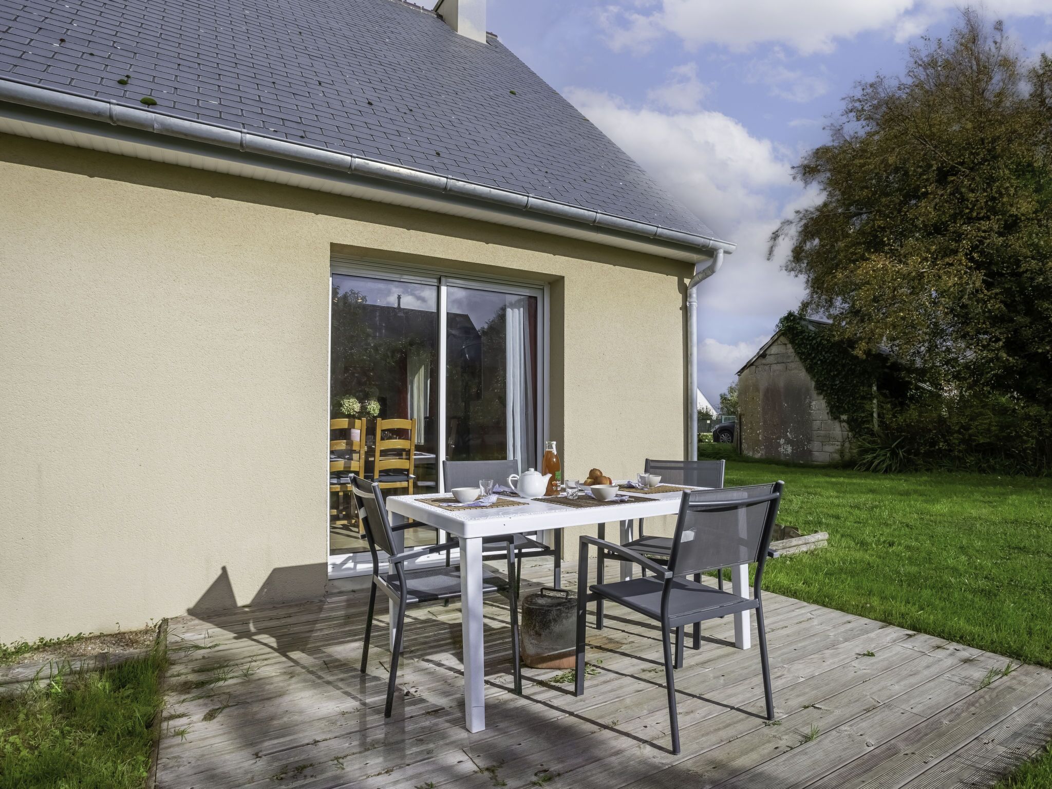 Eine Terrasse im Freien mit Tisch und Stühlen, ein Holzdeck und ein Haus mit Ziegeldach.