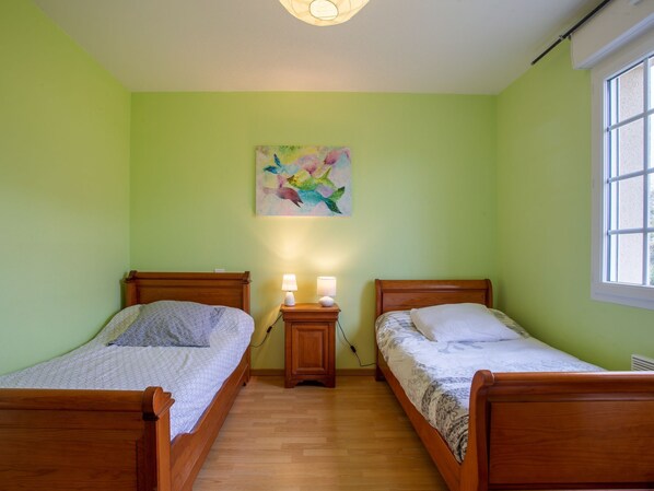 A room with two wooden beds, a nightstand with lamps, a wall-mounted abstract painting, and a window. - Clos d'Amont by Interhome (Portbail)