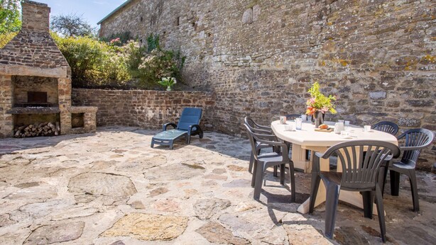 A stone patio with a round table and chairs, a barbecue grill, and a lounge chair. - Le Plongeon by Interhome (Portbail)