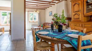A dining area with a wooden table set for four, surrounded by chairs. A chandelier hangs from the ceiling, and a window provides natural light. - Le Plongeon by Interhome (Portbail)