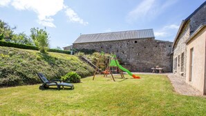 A grassy backyard with a play area, a stone building, and a staircase leading up to a metal-roofed structure. - Le Plongeon by Interhome (Portbail)