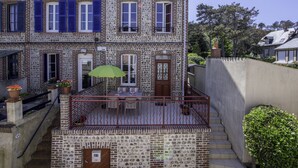 A two-story building with a stone facade, blue shutters, and a small balcony with a green umbrella.