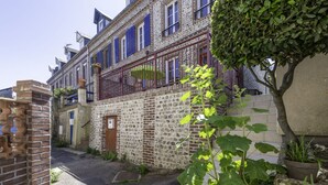 A narrow street with a stone building featuring a balcony with blue shutters.
