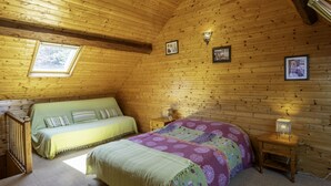 A cozy wooden cabin bedroom with two beds, a skylight, and a small bedside table with a lamp.