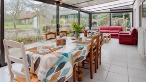 A dining area with a table set for four, surrounded by chairs, and a red sofa in the background. - Les Mésanges by Interhome (St. Lo-d'Ourville)