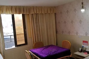 Habitación de hotel con cama, una mesita, una silla, ventana con cortinas y pared con diseño decorativo.