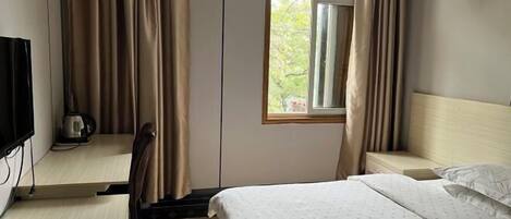 Ein Hotelzimmer mit Bett, Schreibtisch mit Stuhl, einem Fenster mit Vorhängen und einem Fernseher an der Wand.