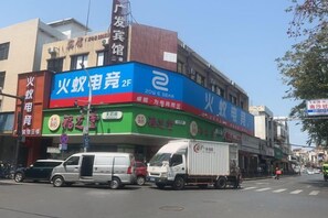A commercial building with multiple storefronts, including a prominent blue and green sign. - Guangfa Hostel (Guangzhou Nansha) (Guangzhou)