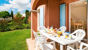 An outdoor dining area with a table set for breakfast, surrounded by white chairs, and a garden in the background. - Port Minervois by Interhome (Homps)