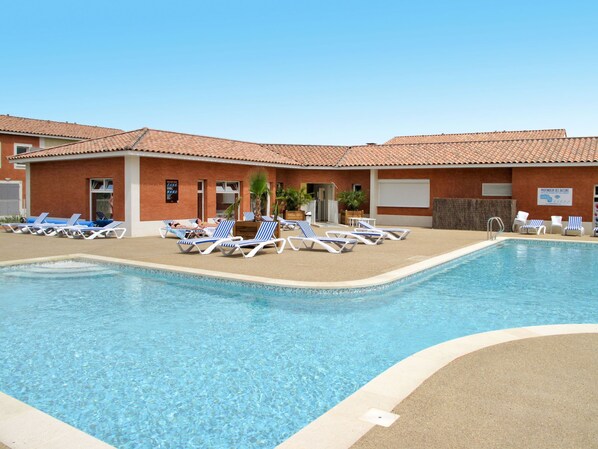 A swimming pool with lounge chairs and a building with a tiled roof.