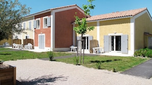 Un bâtiment à deux étages avec une façade rouge et jaune, une allée gravillonnée et des places assises à l’extérieur.