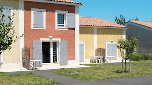 Un bâtiment à deux étages, doté d’un toit recouvert de tuiles, d’une entrée principale avec une porte et d’un petit patio aménagé avec une table et des chaises.
