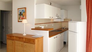 Une cuisine de taille réduite avec des meubles blancs, un plan de travail en bois, un évier et un réfrigérateur.