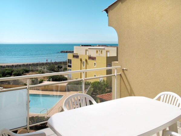 Un balcón con piscina, sillas blancas y vista al mar y edificios.