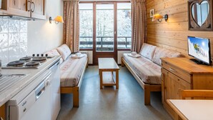 A cozy cabin-style room with a kitchenette, two beds with matching headboards, a wooden dining table, and a television. - Grand Morillon by Interhome (Morillon)