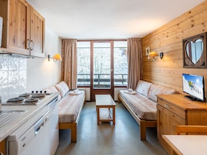 A cozy cabin-style room with a kitchenette, two beds with matching headboards, a wooden dining table, and a television.