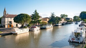 A canal lined with boats and buildings, including a church with a steeple. - Port Minervois by Interhome (Homps)