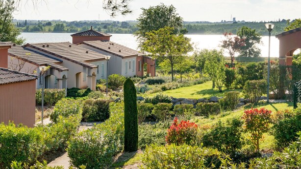 A residential area with houses, a well-maintained garden, and a lake in the background. - Port Minervois by Interhome (Homps)
