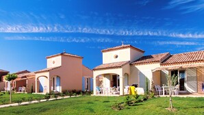 A row of Mediterranean-style villas with terracotta roofs, outdoor seating, and a clear blue sky. - Port Minervois by Interhome (Homps)